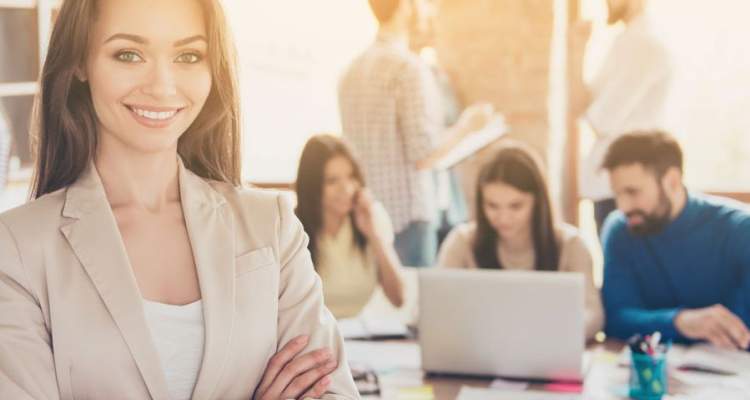 Professional woman in business attire with coworkers in background using laptops