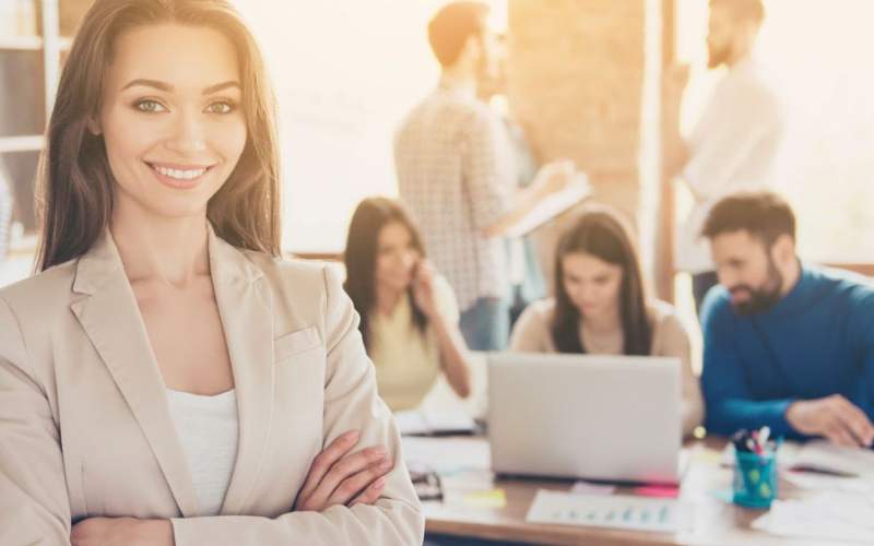 Smiling woman in business attire standing in front of coworkers at a meeting