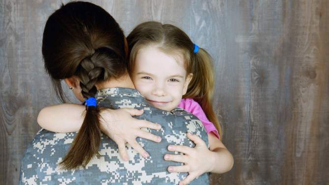 Young child hugging parent in military uniform
